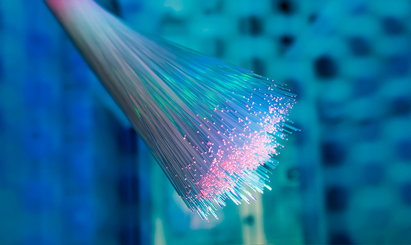 A close-up of glowing fiber optic cables with bright light points at the ends, set against a blurry blue background.