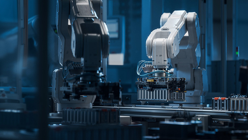 Two robotic arms operate on an assembly line in a modern, high-tech factory, assembling electronic components under blue-toned lighting.