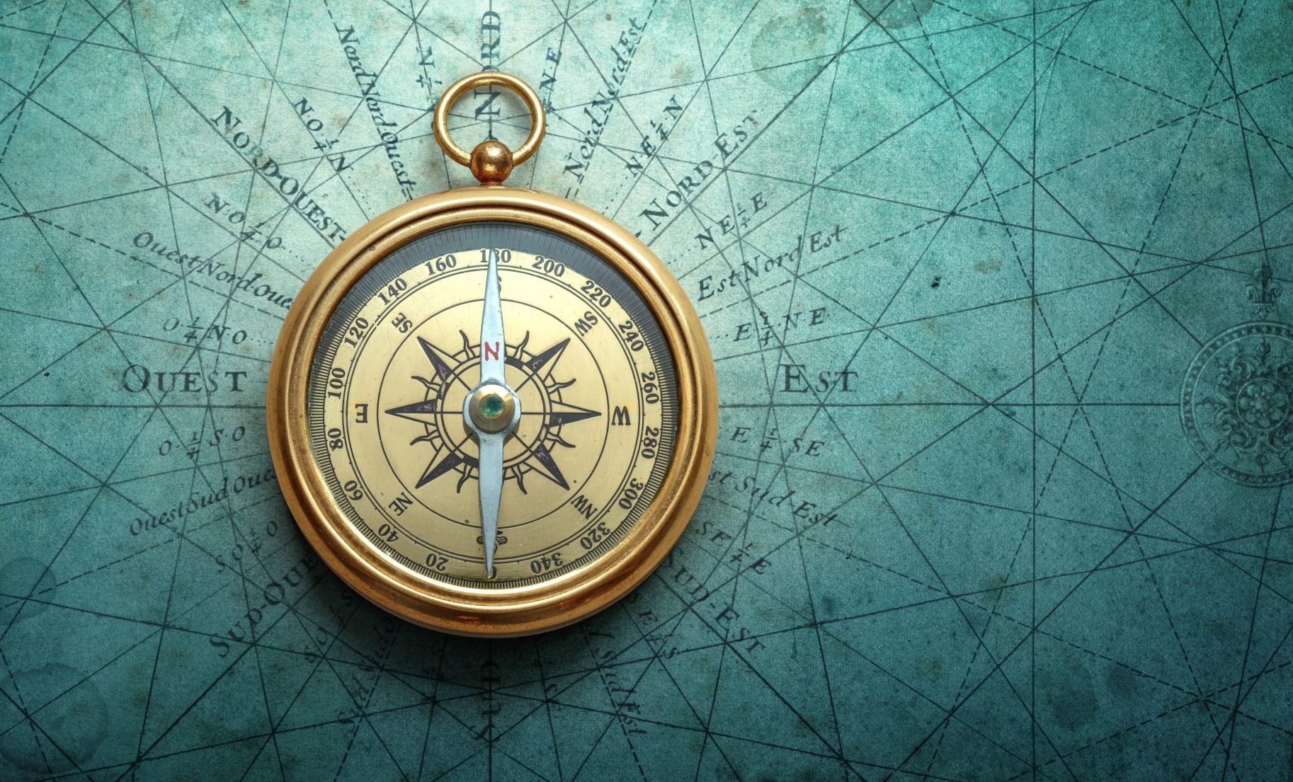 A vintage brass compass rests on an old, blue-green nautical map marked with lines and coordinates, symbolizing navigation and exploration.