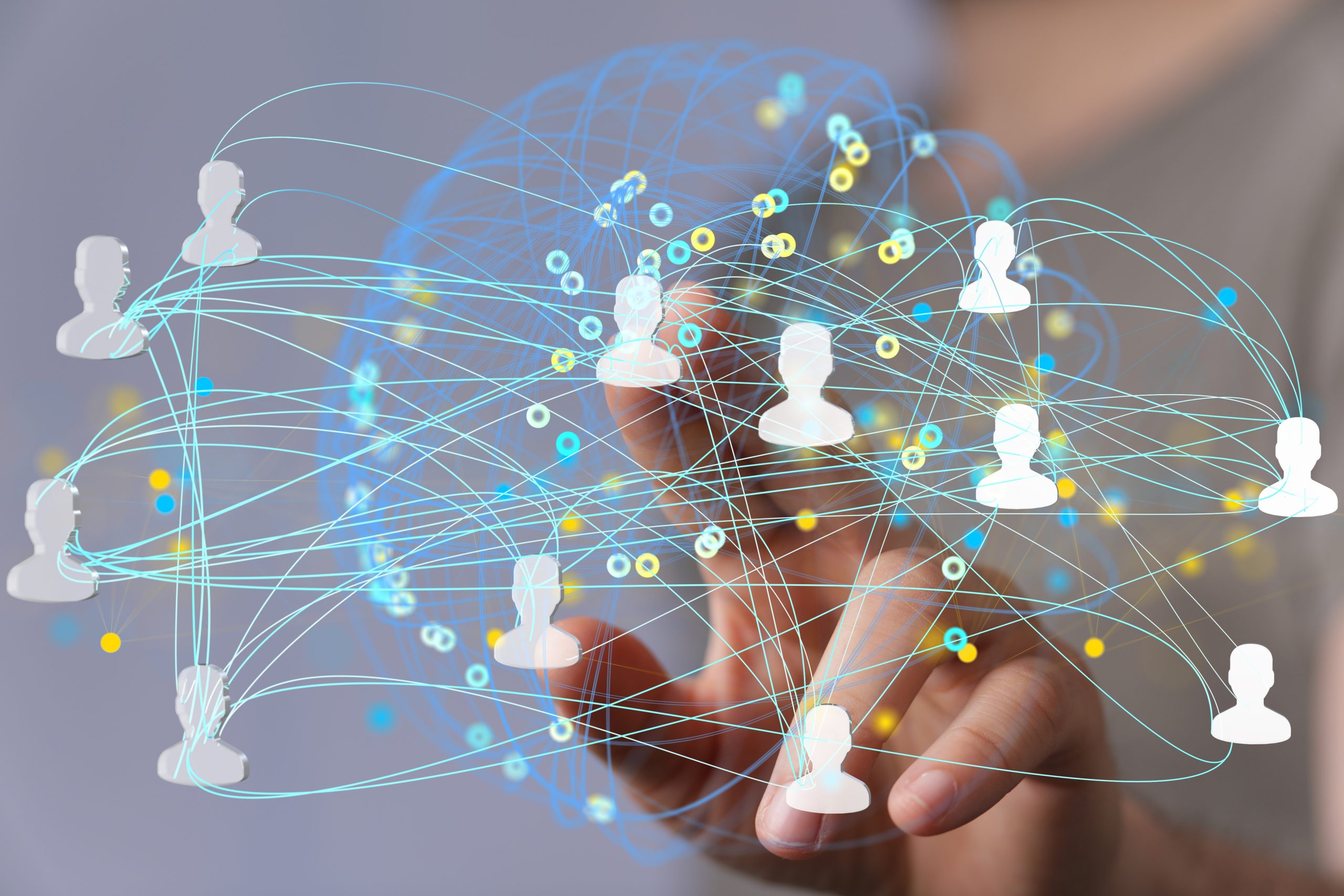 A hand reaching forward, touching virtual icons of connected people, with blue and yellow lines representing a digital network or social connections on a transparent screen.
